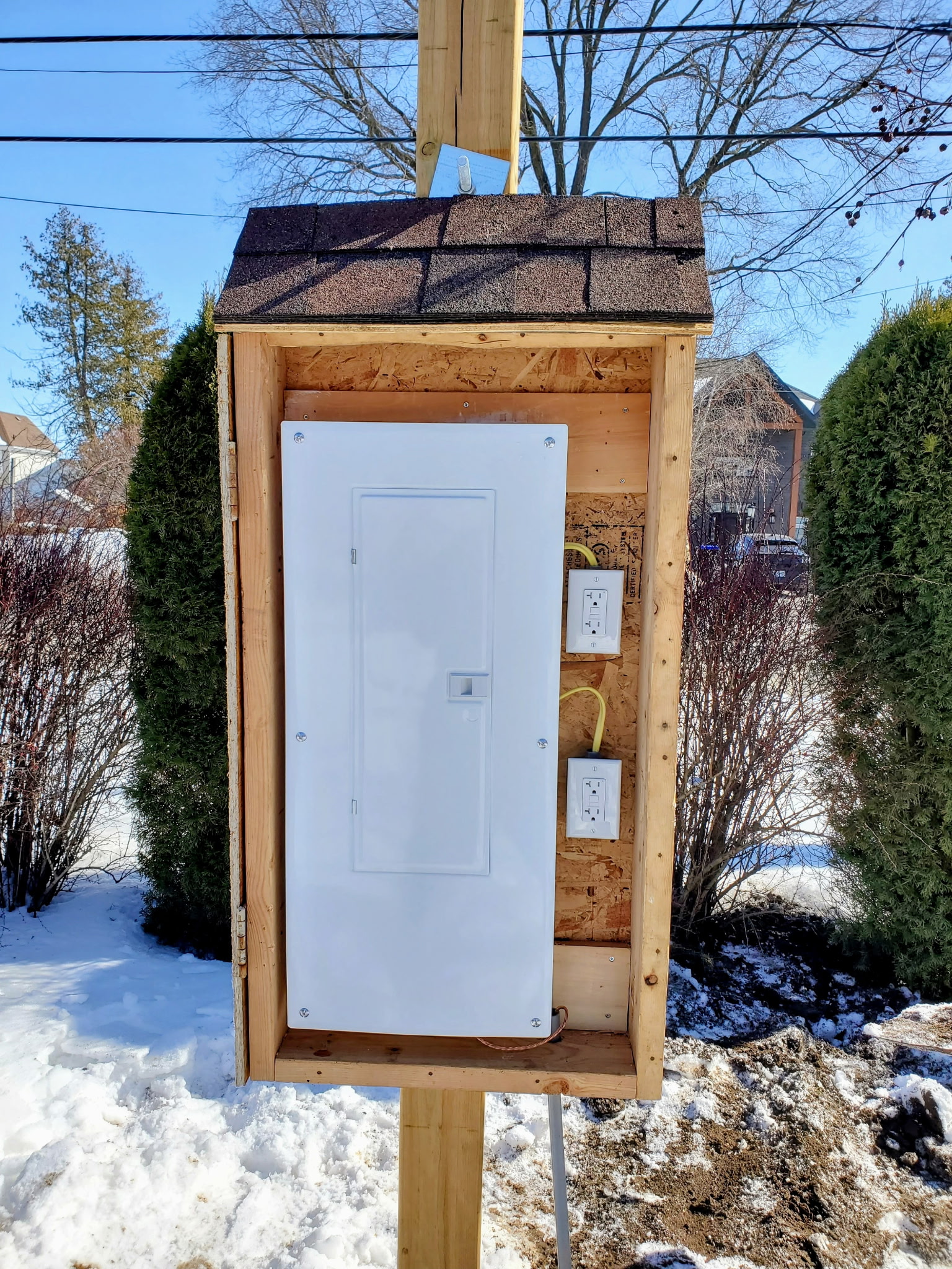 Outdoor panel enclosure with a shingled roof protecting the service
